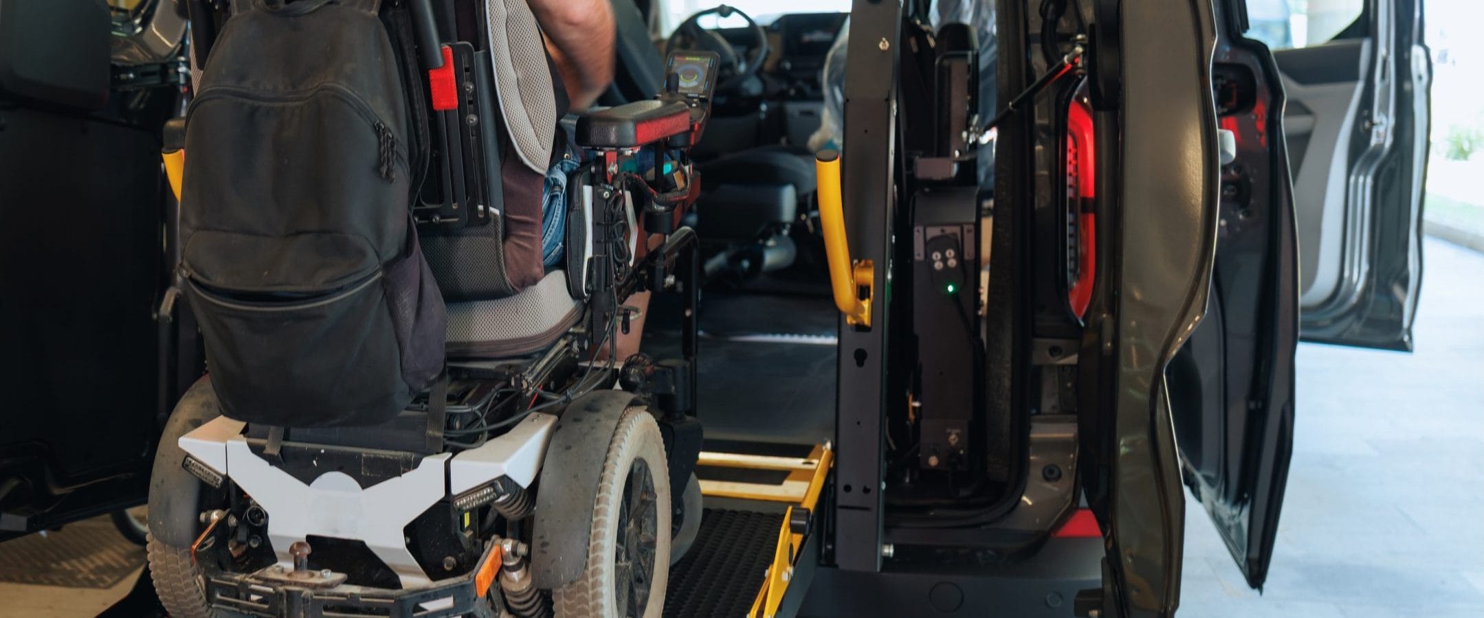 Disabled individual operating a lift on a rear-entry wheelchair van.