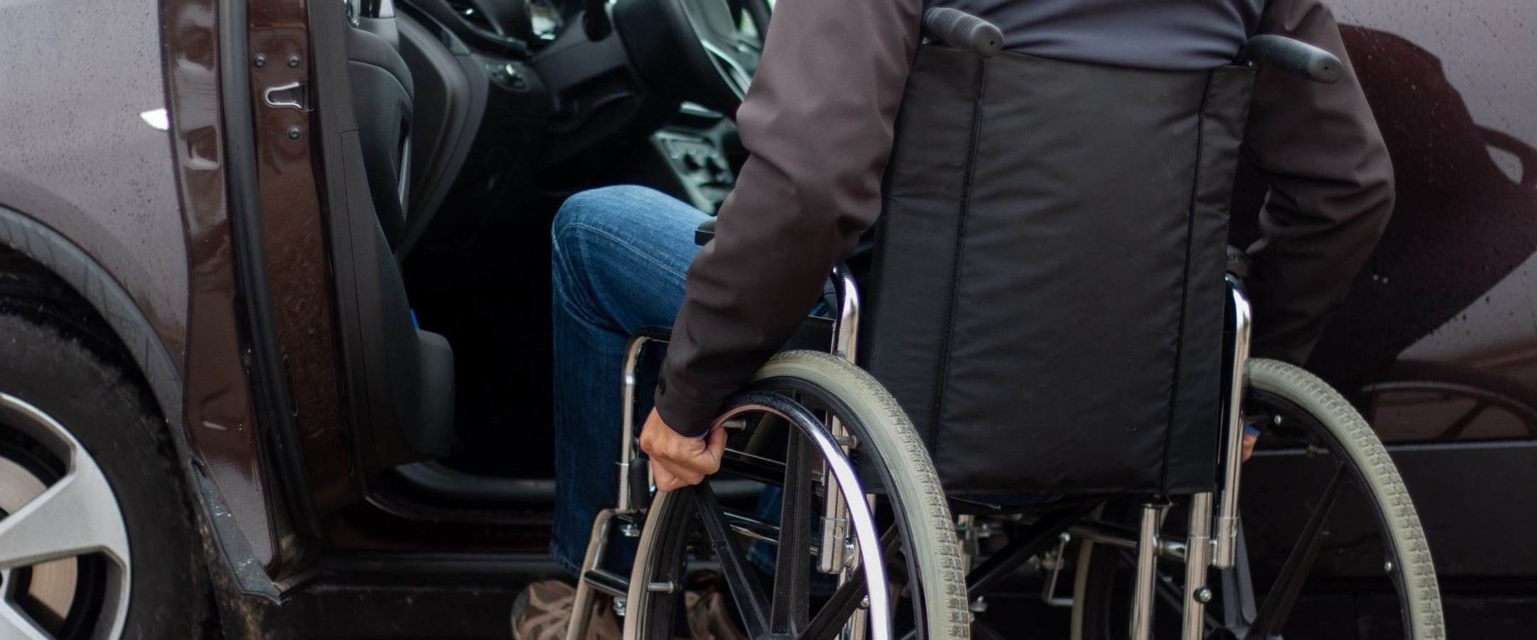 Man in a wheelchair, stopped at the open door on the driver's side, preparing to get in.