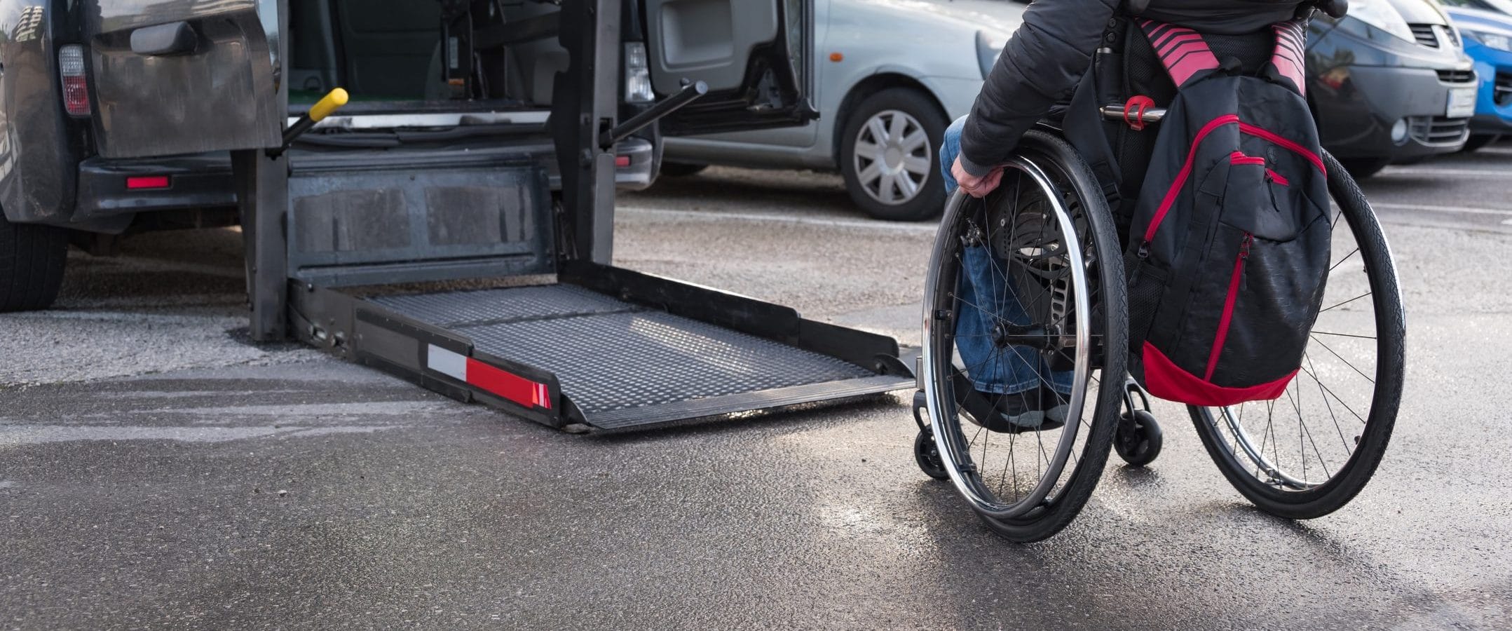 Person in a wheelchair going toward a lift on the back of an accessible vehicle to get in.