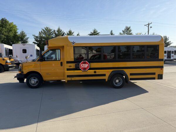 Yellow school bus parked in a lot, stop sign extended on the side, with other buses and trees in the background under a clear blue sky.