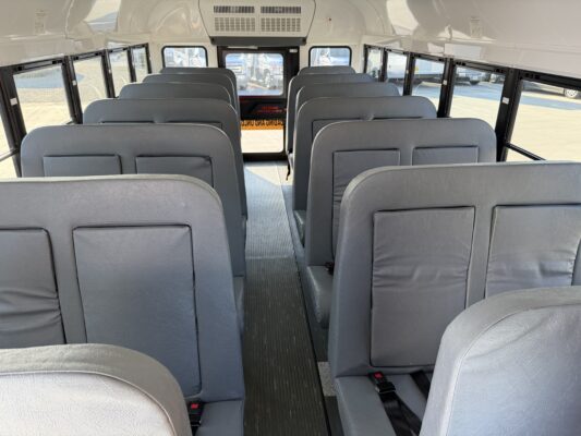 Interior of a school bus with gray vinyl seats, long central aisle, windows on both sides, daylight outside.