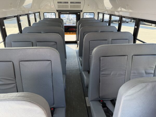 Interior of a school bus with gray vinyl seats, long central aisle, windows on both sides, daylight outside.