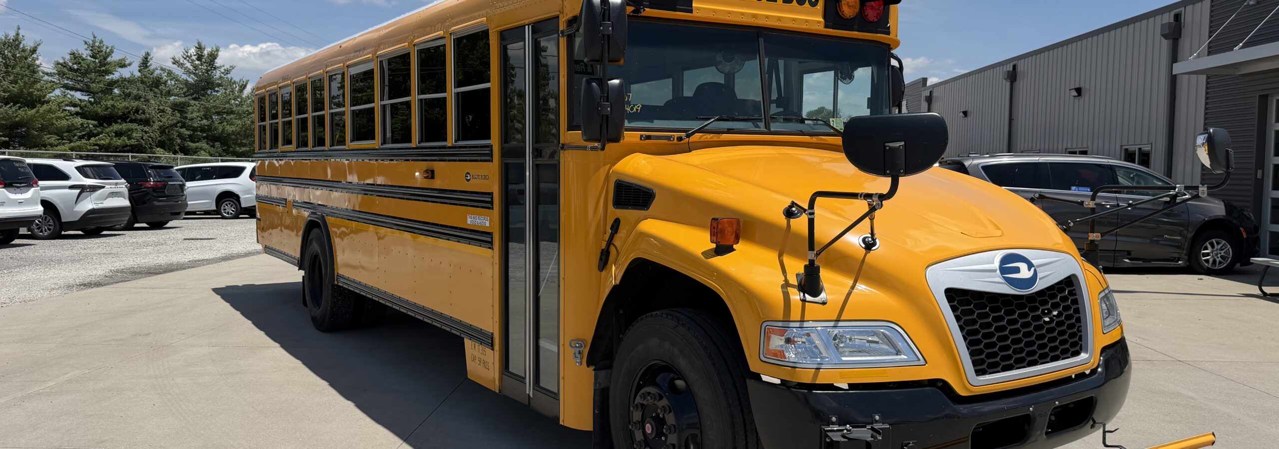 Front view of a yellow school bus parked in a lot, with a prominent 'SCHOOL BUS' sign on the top edge of the bus hood.