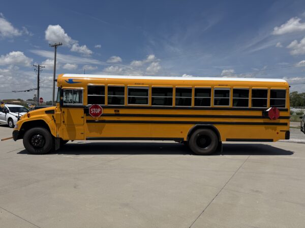 Yellow school bus parked in a lot with a stop sign and power lines under a blue sky with clouds.