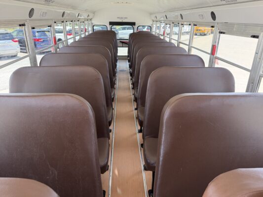 Inside a school bus with brown seats arranged in rows, a central aisle, and windows on both sides