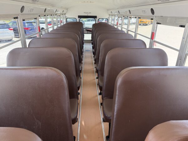 Inside a school bus with brown seats arranged in rows, a central aisle, and windows on both sides