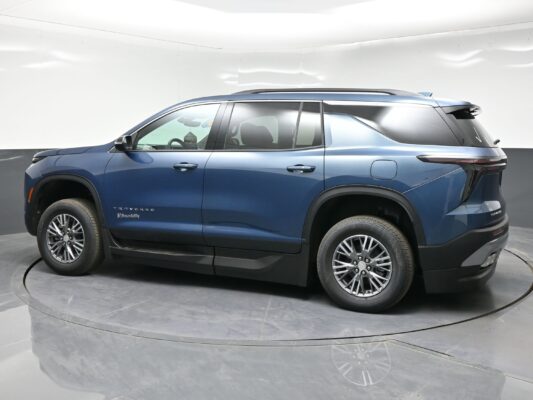 Blue Chevrolet Traverse SUV shown in a side profile in a showroom or studio setting, focusing on the midsection and wheels, with a white backdrop.