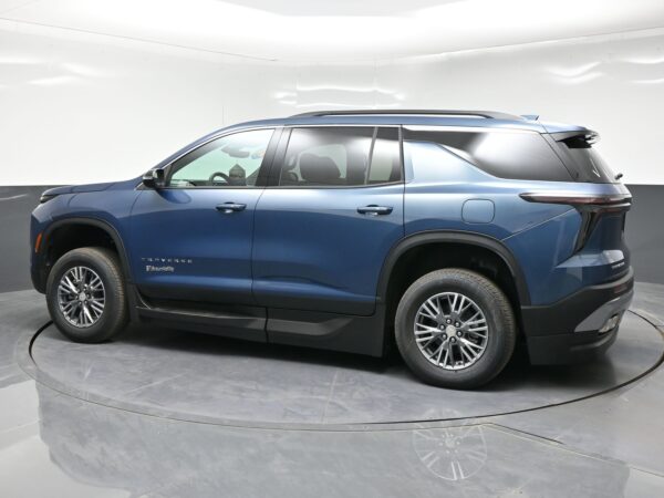 Blue Chevrolet Traverse SUV shown in a side profile in a showroom or studio setting, focusing on the midsection and wheels, with a white backdrop.