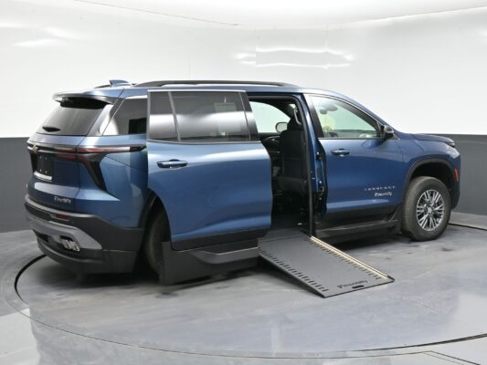 Blue Chevrolet Traverse SUV with the passenger-side door open and a BraunAbility wheelchair ramp extended inside a showroom.