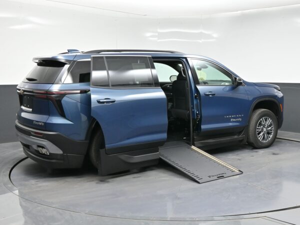 Blue Chevrolet Traverse SUV with the passenger-side door open and a BraunAbility wheelchair ramp extended inside a showroom.
