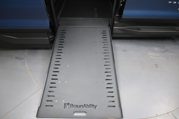 Blue van with a BraunAbility ramp extended to the ground on a gray garage floor.