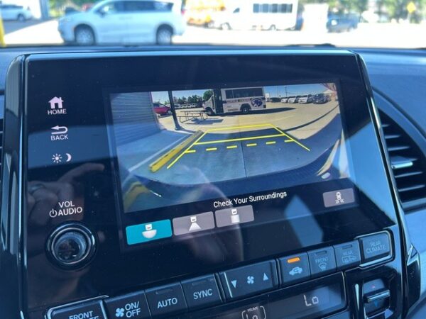 Backup camera Rearview camera display showing yellow parking guidelines on a car’s touchscreen as you back into a spot, with surrounding dashboard controls visible below.