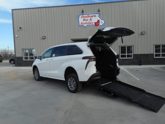 White SUV with a deployed wheelchair ramp in a parking lot in front of a gray industrial building with a Southern Bus & Mobility sign nearby.