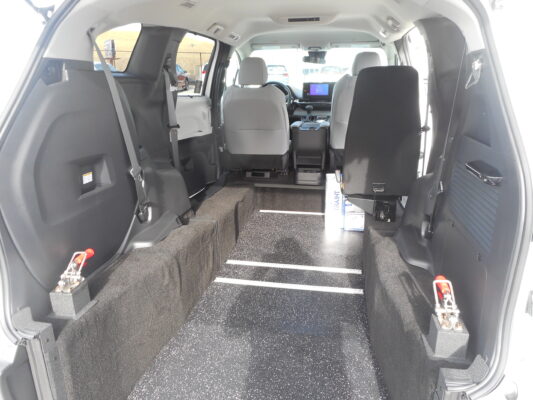 Interior of a vehicle's rear cargo area with carpeting, tie-downs, and folded second-row seats visible toward the front.
