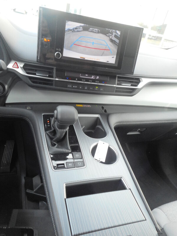 DSCN3748 Car interior center console with gear shift, cup holder, and a touchscreen displaying the rear-view backup camera in a parking lot with guide lines.
