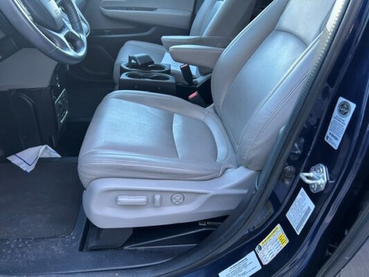 Interior of a vehicle showing the driver's seat with light gray leather, center console, and steering wheel.