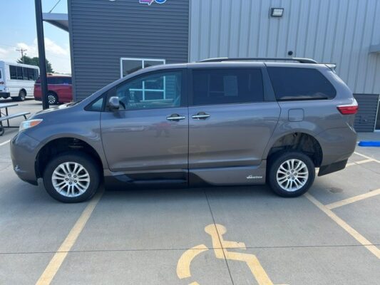 Gray minivan parked in a handicap parking space in front of a commercial building/ dealership.