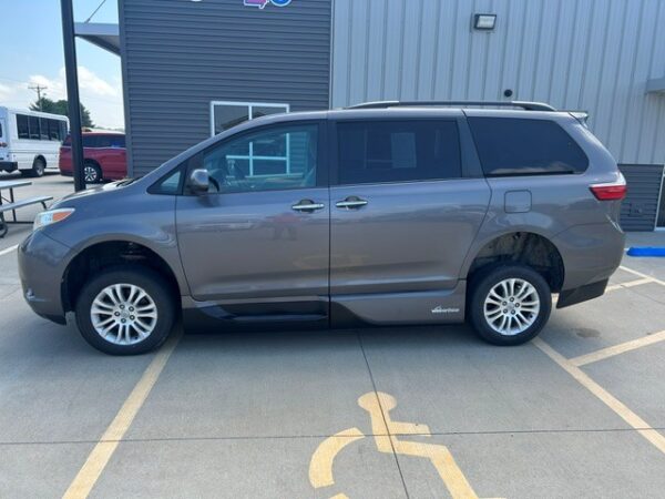 Driver's side Gray minivan parked in a handicap parking space in front of a commercial building/ dealership.
