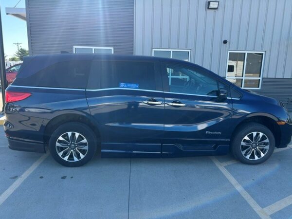Passenger side view Blue minivan parked in a parking lot beside a metal industrial building, shown in full side view with sliding doors and alloy wheels.