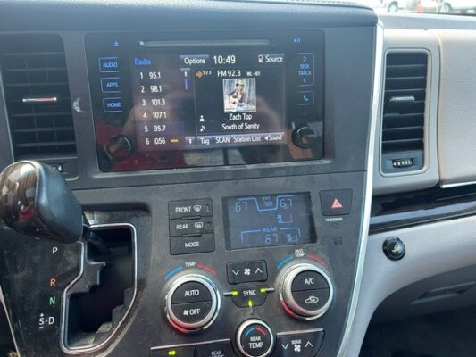 Center console of a car showing a touchscreen infotainment display (radio) with climate controls below and a gear shifter to the left.