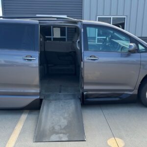 Gray minivan with a deployed wheelchair ramp extending from the side door, parked in a lot.
