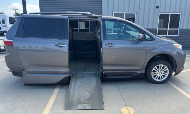 Gray minivan with a deployed wheelchair ramp extending from the side door, parked in a lot.