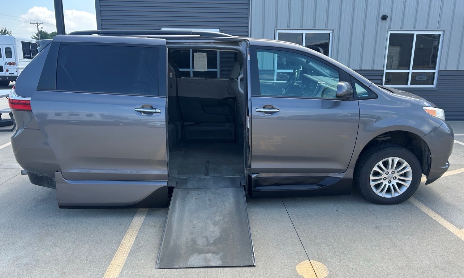 Gray minivan with a deployed wheelchair ramp extending from the side door, parked in a lot.