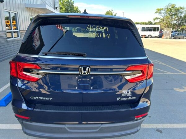Rear View Blue Honda Odyssey SUV viewed from the rear in a parking lot; badges show 'Odyssey' and BraunAbility logo, with yellow writing on the rear window.