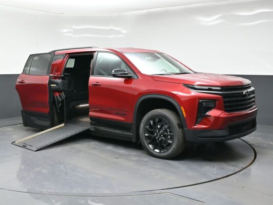 Red Chevrolet Traverse with a deployed side ramp for wheelchair access, doors open, in a showroom setting