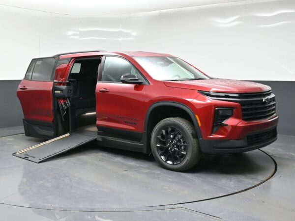 Red Chevrolet Traverse with a deployed side ramp for wheelchair access, doors open, in a showroom setting