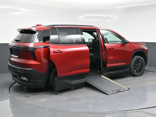 Red SUV with a side-entry ramp lowered and door open, showing a wheelchair-accessible modification in a showroom setting.