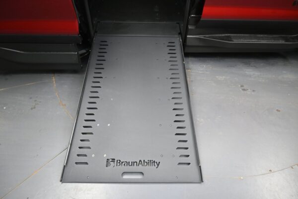 Wheelchair ramp extended from a red BraunAbility vehicle, metal surface with side slots for grip control and branding visible.