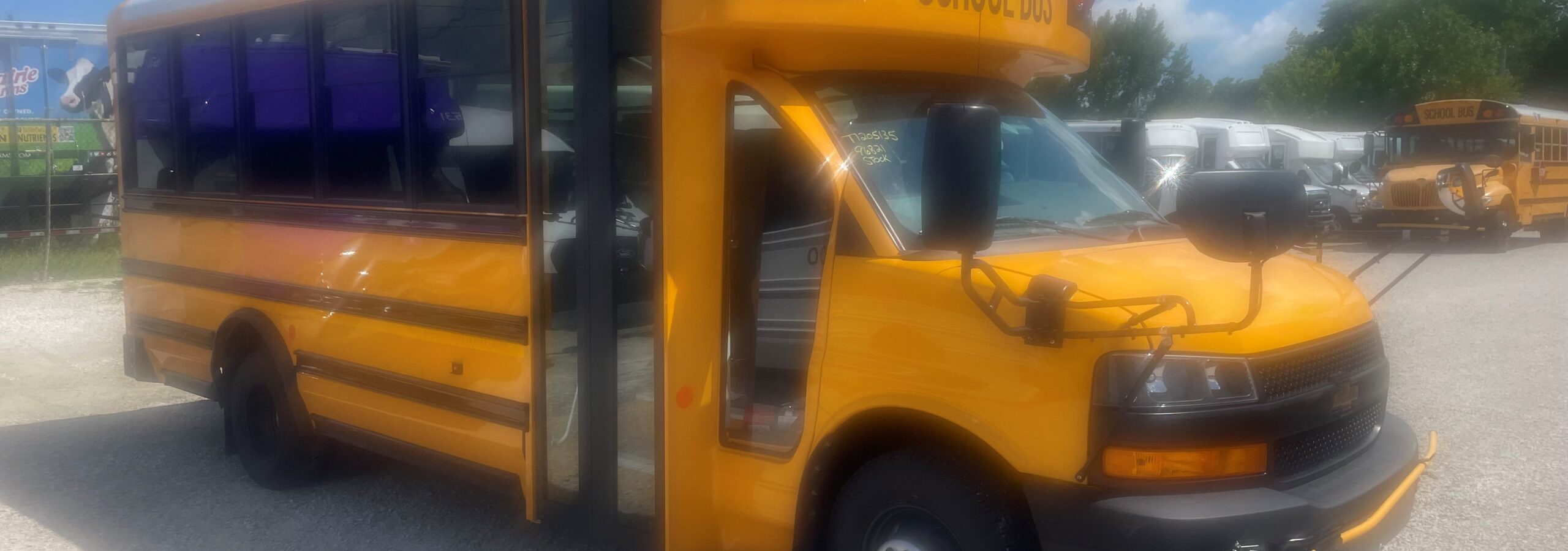 Yellow school bus with its door open, parked in a lot under a blue sky with clouds.