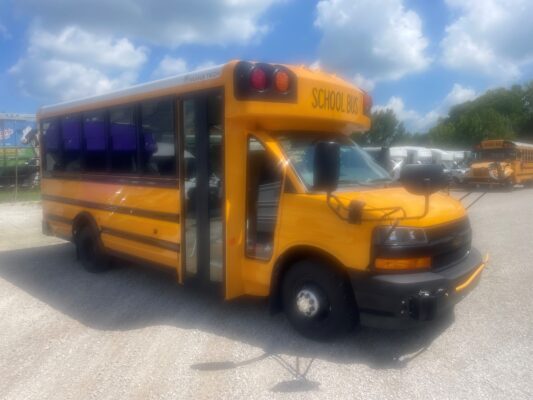 Yellow school bus with its door open, parked in a lot under a blue sky with clouds.
