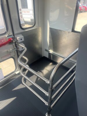 Inside a bus near the door, shiny stainless steel handrails and vertical rails with textured black lower panels.