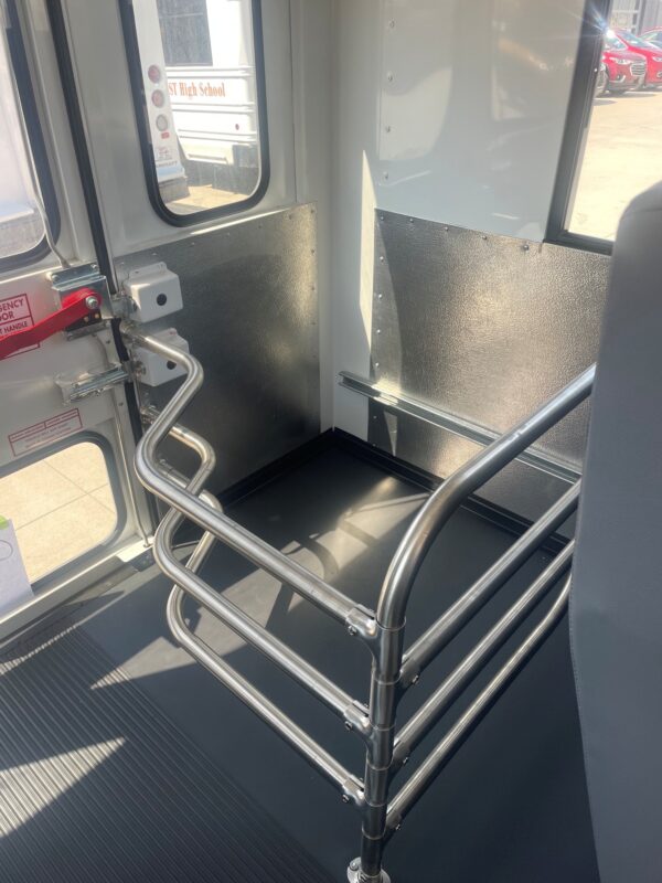 Inside a bus near the door, shiny stainless steel handrails and vertical rails with textured black lower panels.