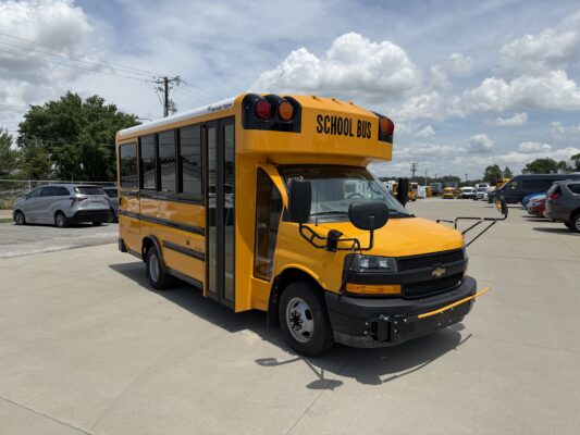 Front-right view of a yellow school bus in a parking lot with other vehicles nearby, 'SCHOOL BUS' markings visible on the front.