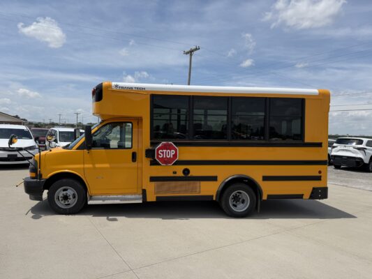 Yellow school bus with a stop sign on the side, parked in a lot under a blue sky with power lines in the background.