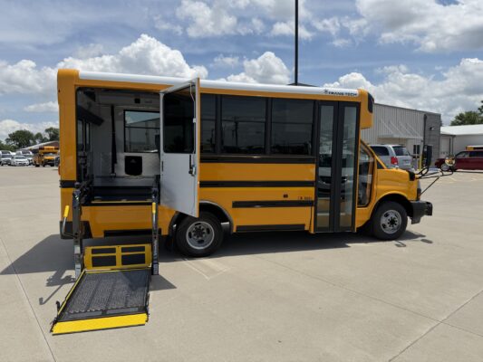 Yellow school bus with a lowered wheelchair ramp extended for accessible boarding in a sunny parking lot