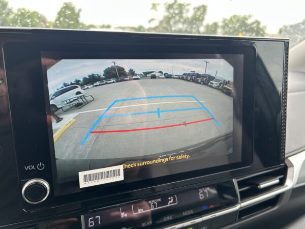 IMG_4981 Rearview camera screen showing a parking lot with blue guiding lines to assist reversing and a safety message below.