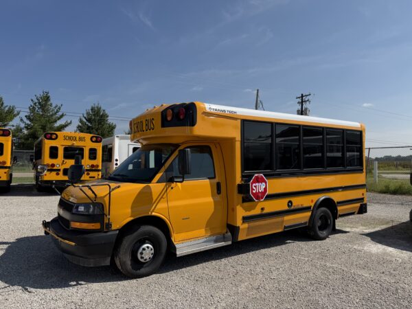 Front and side view of a yellow school bus with a STOP sign extended, other buses in the background under a clear blue sky.