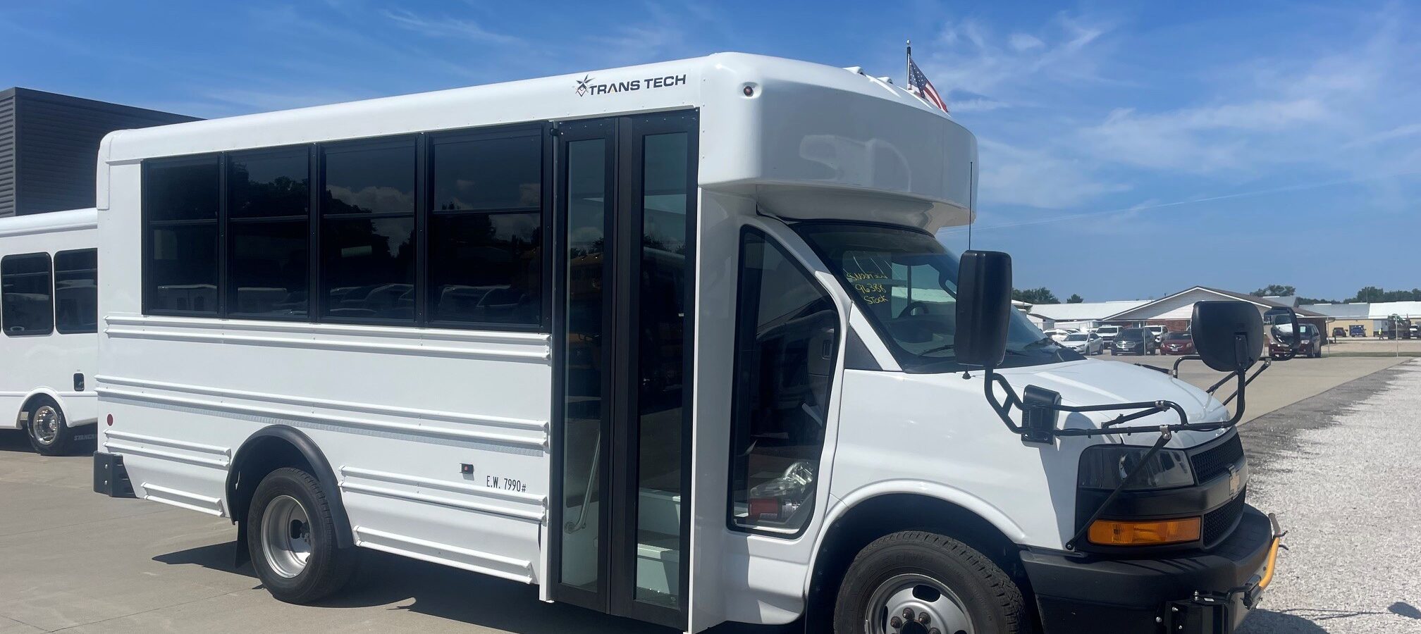 White shuttle bus with large windows and ‘TRANS TECH’ logo on the side, parked under a blue sky.