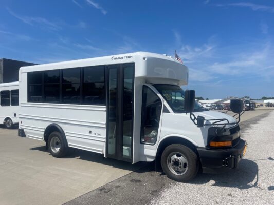White shuttle bus with large windows and ‘TRANS TECH’ logo on the side, parked under a blue sky.