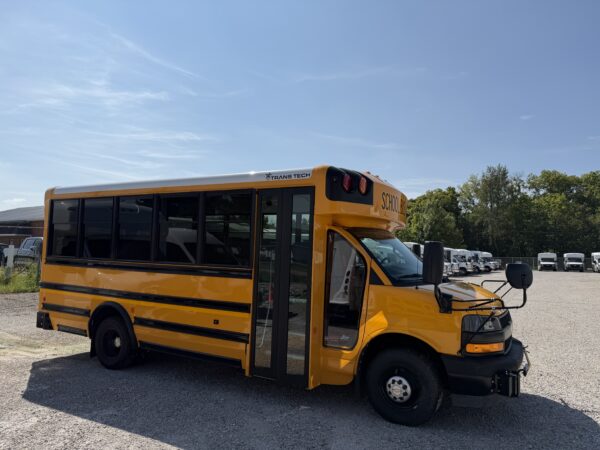 Yellow school bus parked in a lot, showing the side and front with trees and blue sky in the background