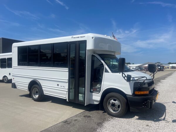 White shuttle bus with large windows and ‘TRANS TECH’ logo on the side, parked under a blue sky.