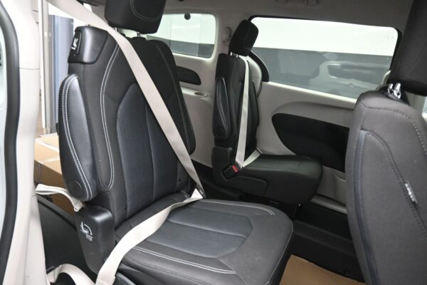 Interior of a vehicle showing two black captain's chairs with white stitching, beige seat belts, and light gray door panels.