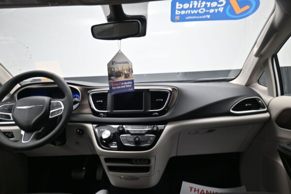 Front interior of a car showing steering wheel, center console, and a BraunAbility tag hanging from the rearview mirror.