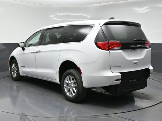 White Chrysler Voyager minivan shown from a rear three-quarter angle, with visible taillights, back hatch, and roof spoiler in a studio setting.