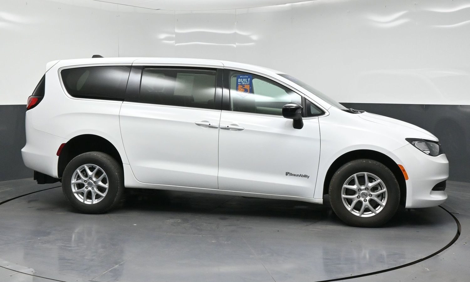Profile view of a white minivan in a studio setting, BraunAbility branding on the front door area