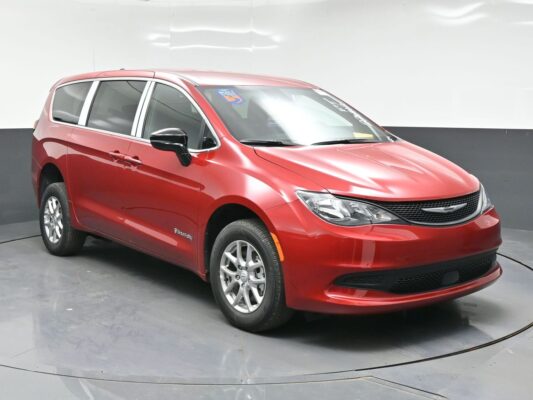 Red minivan (Chrysler Pacifica) parked indoors on a turntable display, facing right with tinted windows and chrome accents.